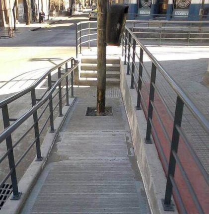 A pole blocking a wheelchair ramp.
