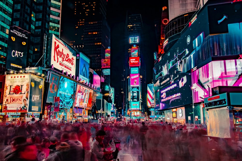 Time square in New York at night. Bright billboards on the buildings. A motion blur of people on the street.